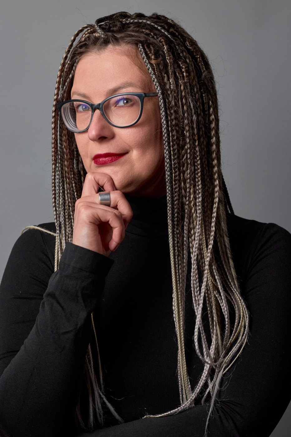 Portrait of a woman with braids and glasses, hand at her chin